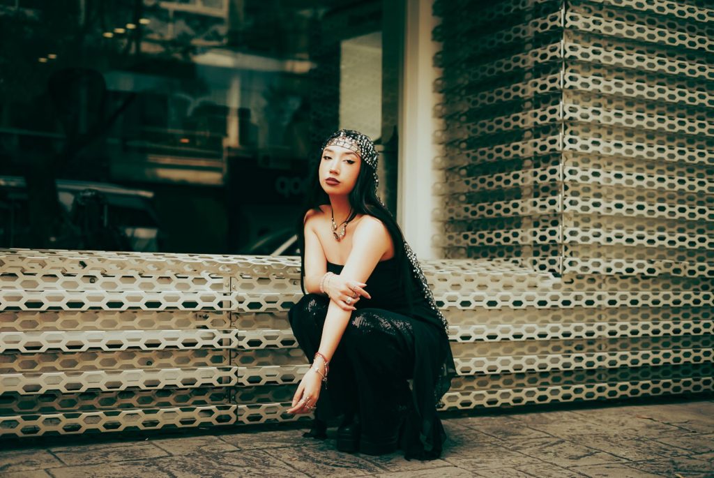 Femme en tenue noire urbaine, mélange de textures et accessoires brillants